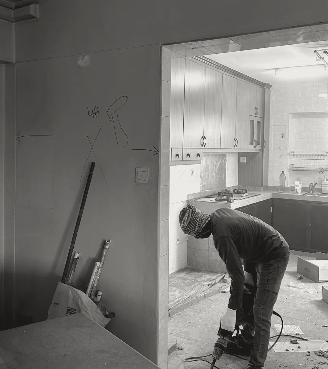 An HDB kitchen mid-hack, with the designer's marker plan drawn on the living room wall and a worker breaking up the kitchen floor.